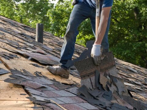 A person with gloves on standing on the roof of a house.