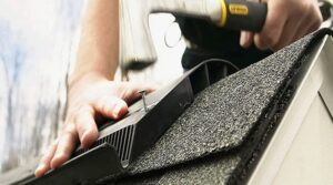 A person using an electric drill on the roof of a house.